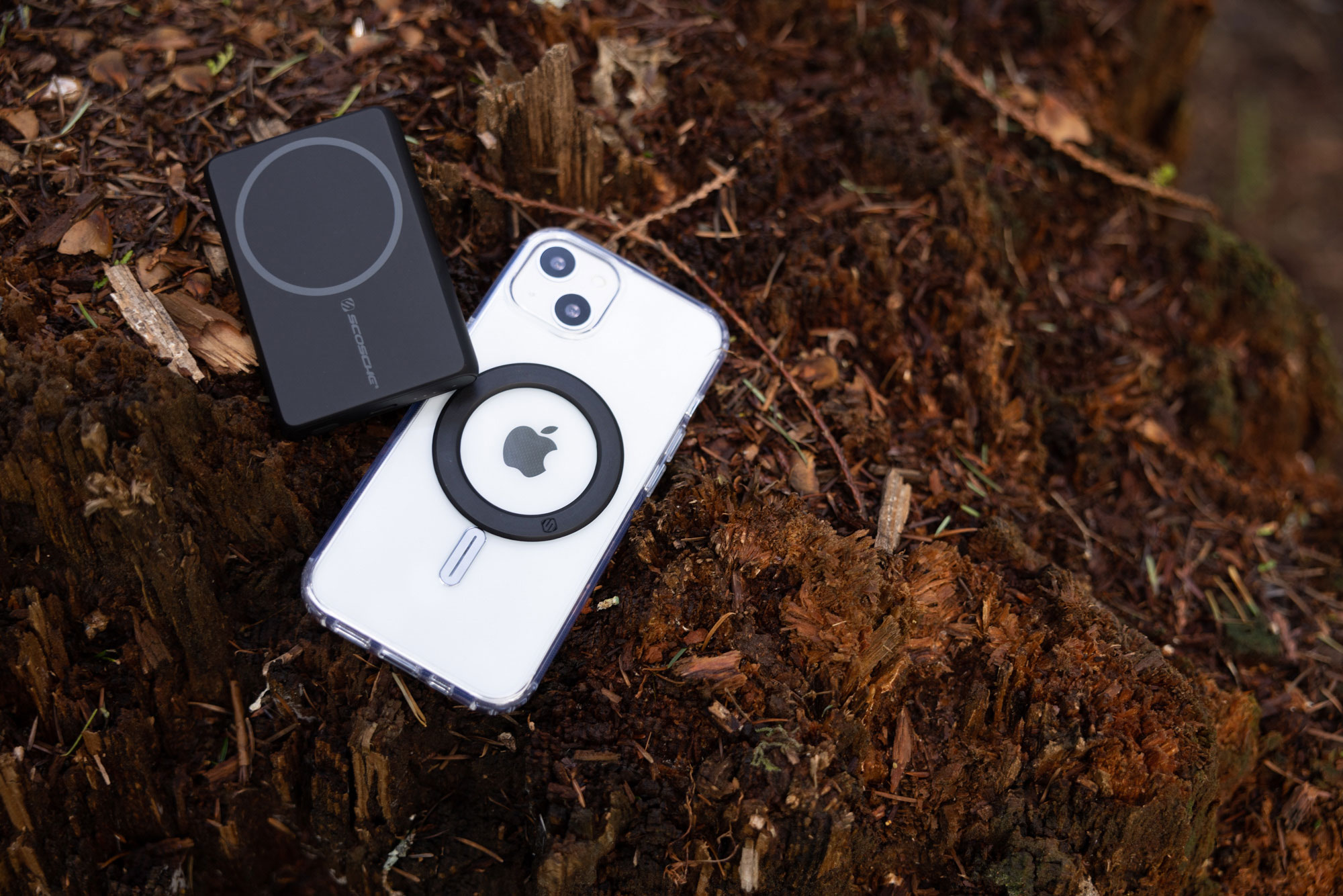 iphone with magic ring adapter next to magsafe portable power bank while laying in forest floor