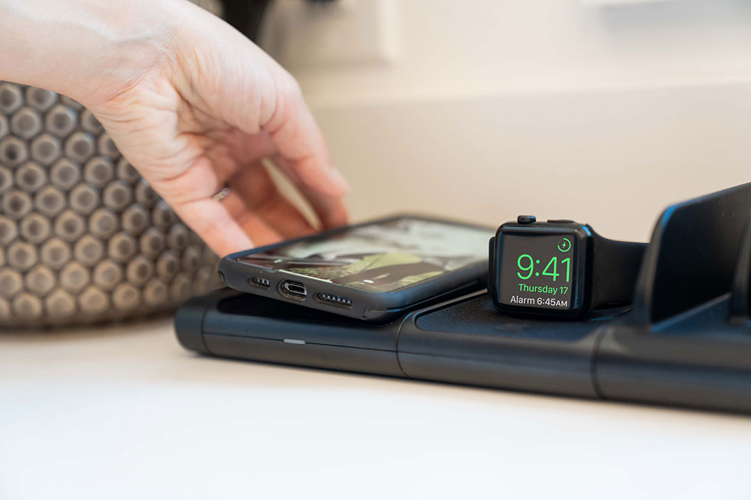 Woman placing iphone on wireless charging pad next to apple watch charging on wireless charger