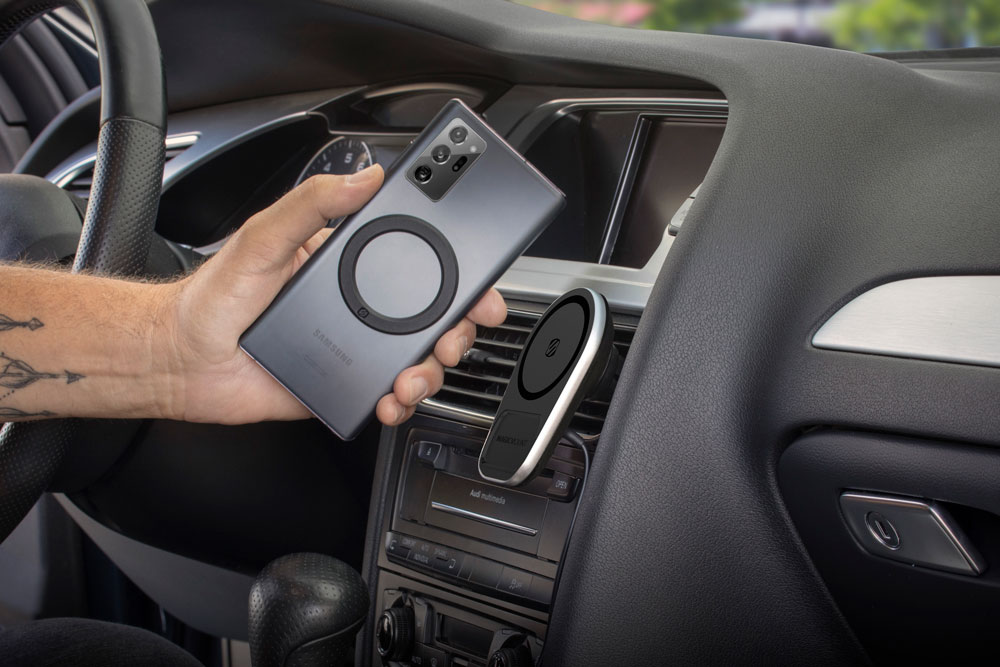 man holding phone with Scosche magic ring adapter for mounting to wireless vent mounted charger in car