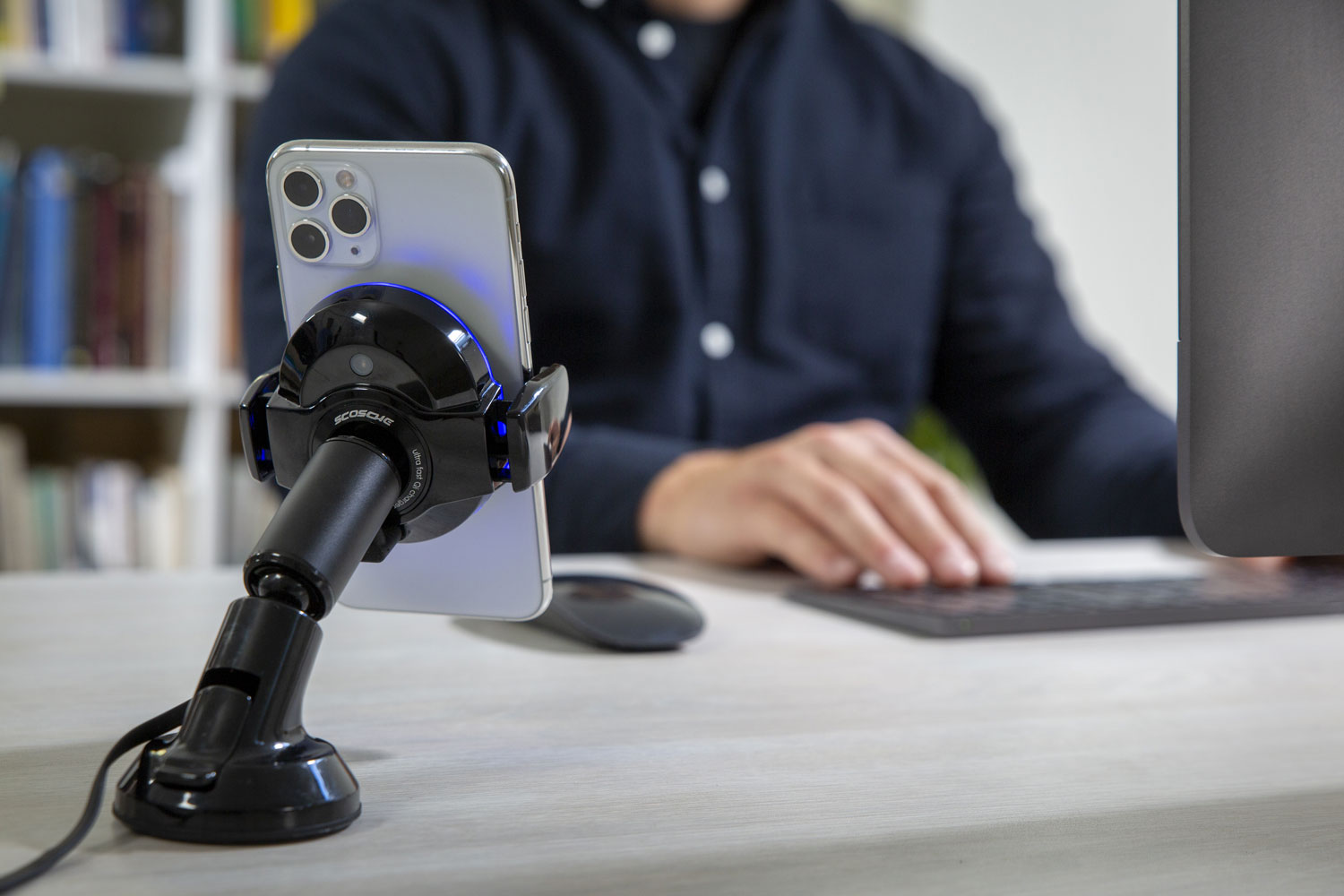 iphone charging via Scosche magic grip wireless charging mount on desk with man sitting at computer in background