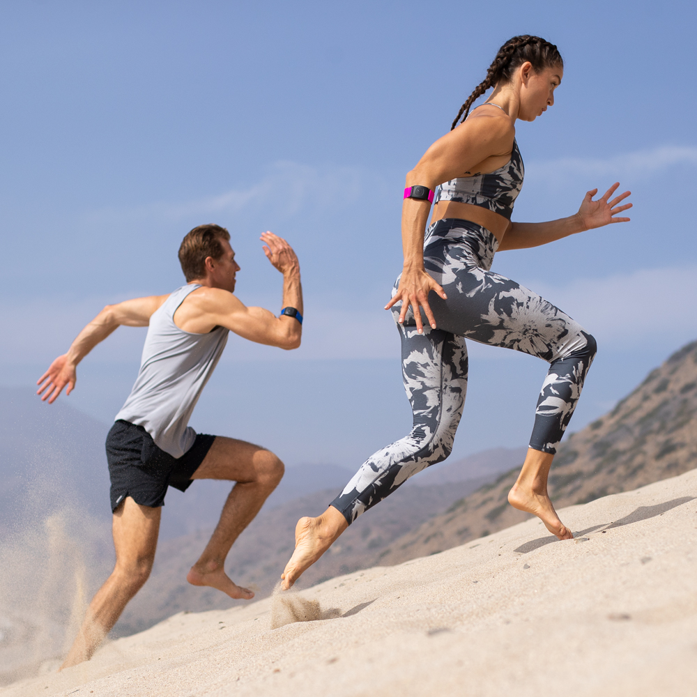 running in sand man and woman running in sand wearing Scosche armband heart rate monitors